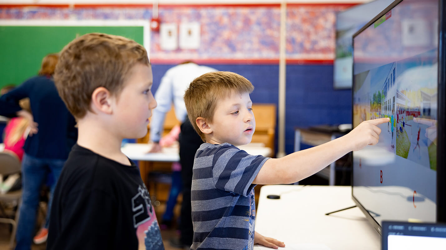 Elementary student points at a screen in a collaborative classroom setting