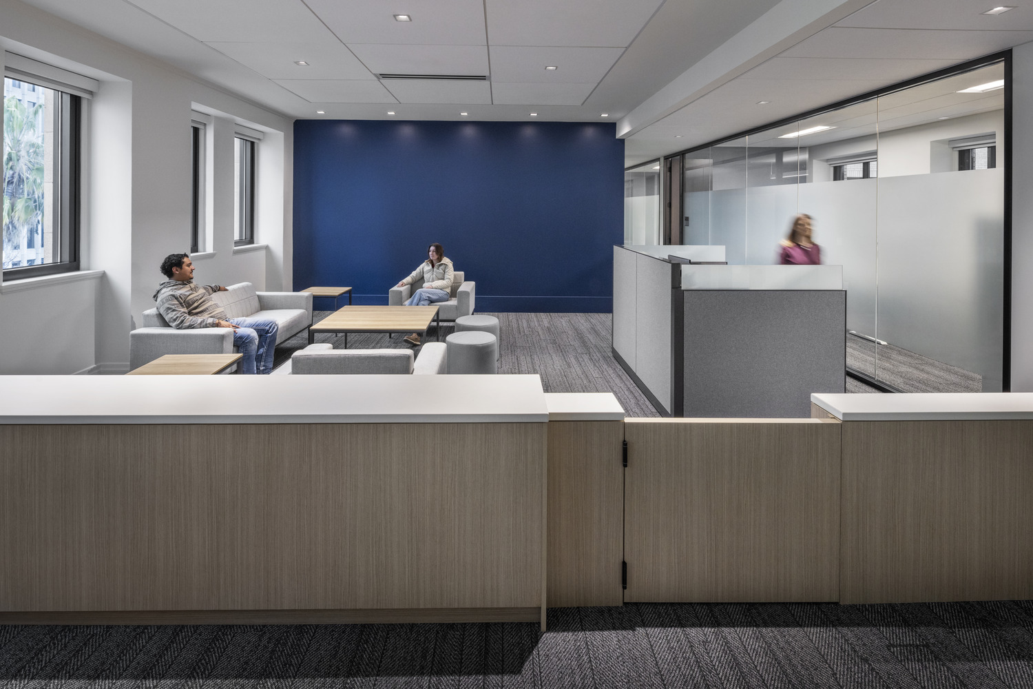 Renovated Jesse Unruh State Office Building lounge with modern seating, glass-walled offices, and a blue accent wall.
