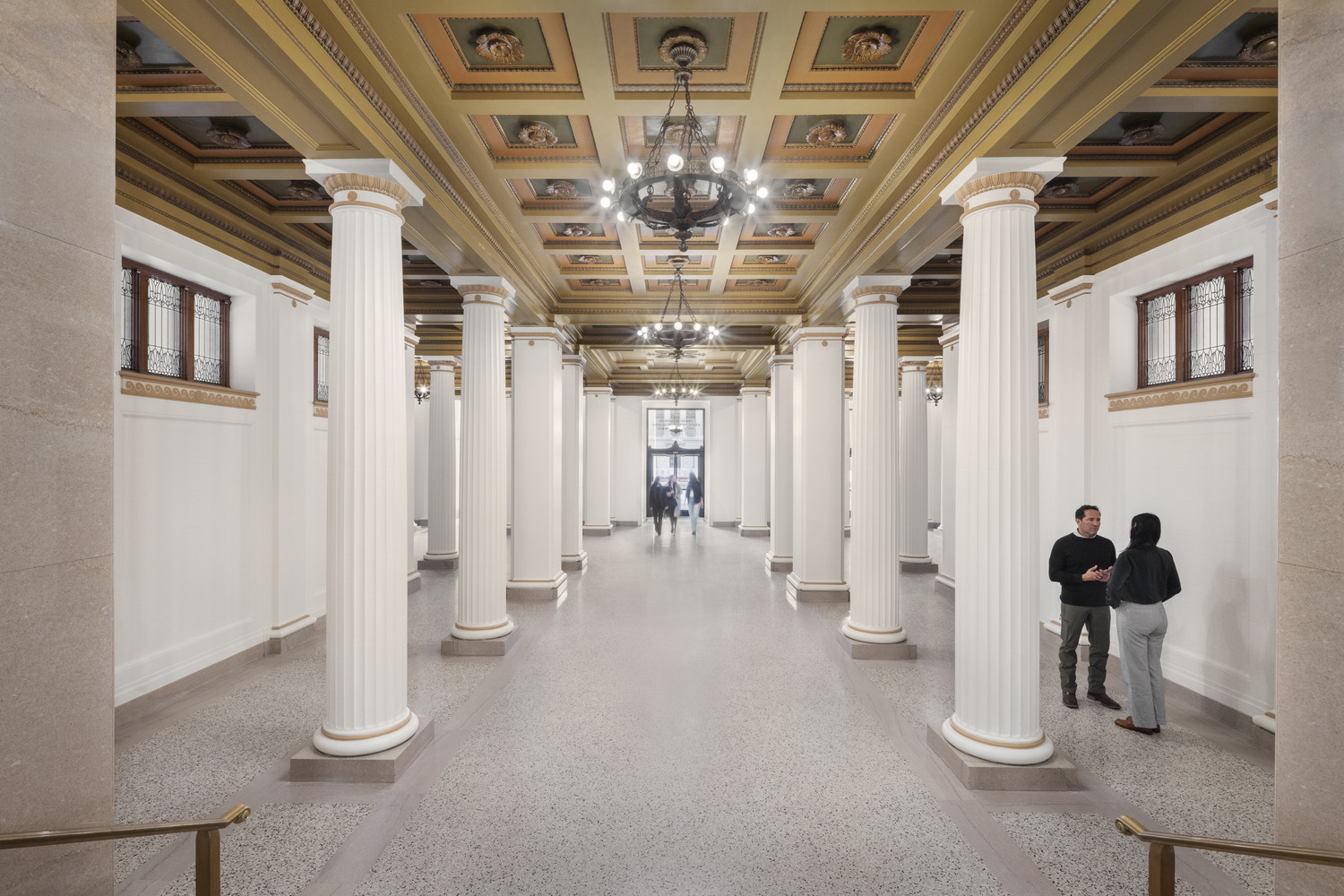 Restored historic lobby of the Jesse Unruh State Office Building, featuring classical columns, ornate ceilings, and chandeliers.