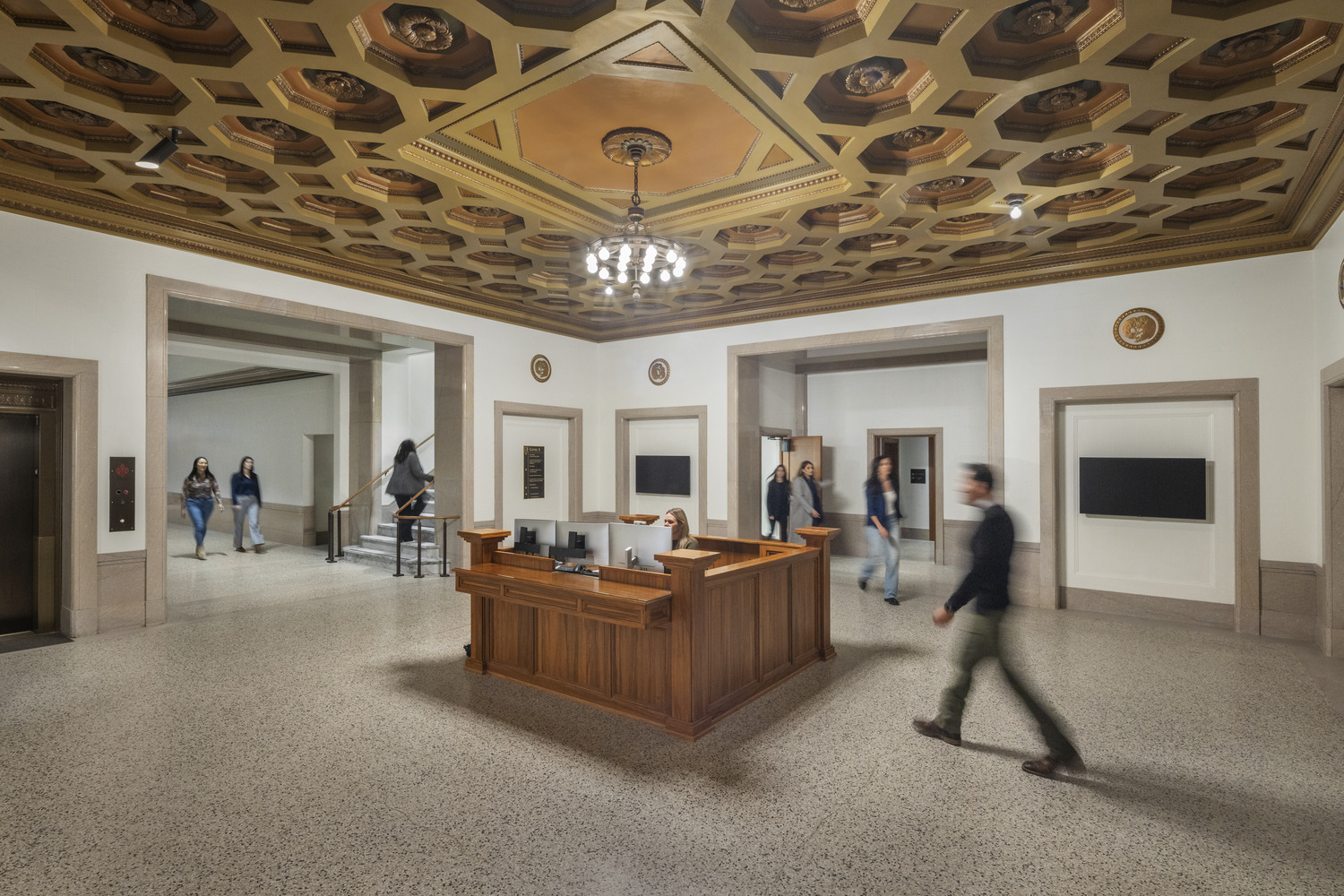 Historic first-floor lobby desk at the renovated Jesse Unruh State Office Building, featuring wood paneling and an ornate coffered ceiling.