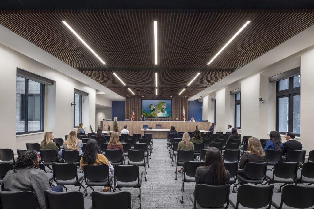 Renovated hearing room at the Jesse Unruh State Office Building with audience seating, a raised dais, and wood-slat ceiling.