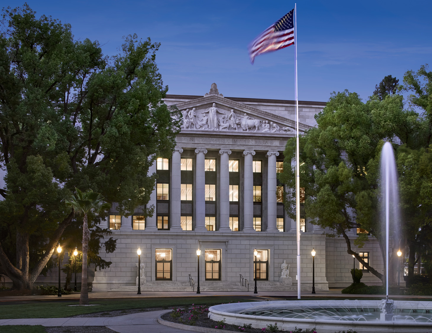Jesse Unruh State Office Building in Sacramento at dusk, featuring classical columns, sculpted pediment, and fountain.