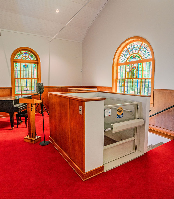 An interior photo of a church sanctuary after it was rehabilitated with a lift in the foreground and a piano and stairs in the background.