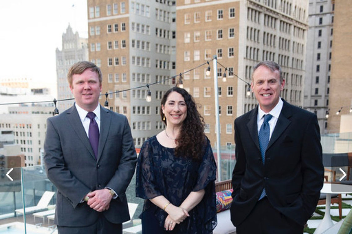 A woman standing between two men in front of historic buildings in Dallas