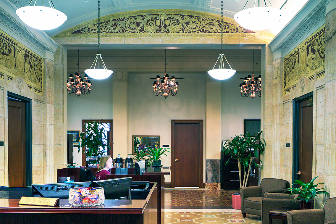 Close-up of a polished balustrade post and corridor view revealing bas-relief murals, ornate metalwork, and vaulted ceilings. The craftsmanship highlights the care taken in both public and transitional spaces, honoring the building’s civic legacy.